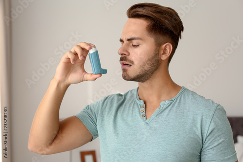 Young man using asthma inhaler at home photo