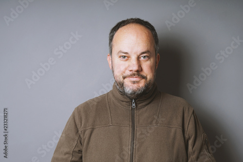 middle aged man in his 40s with short dark hair and graying beard smiling against gray wall with copy space photo