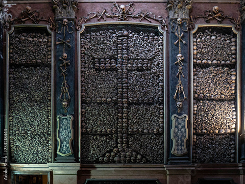 Large pile of real human skulls and bones stacked on a wall to form a christian cross in the ossuary of the church San Bernadino alla Ossa in Milan, Italy