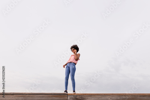 Happy young beautiful afro american woman smiling and talking on her mobile phone. cloudy background. Spring or summer season. Casual clothing