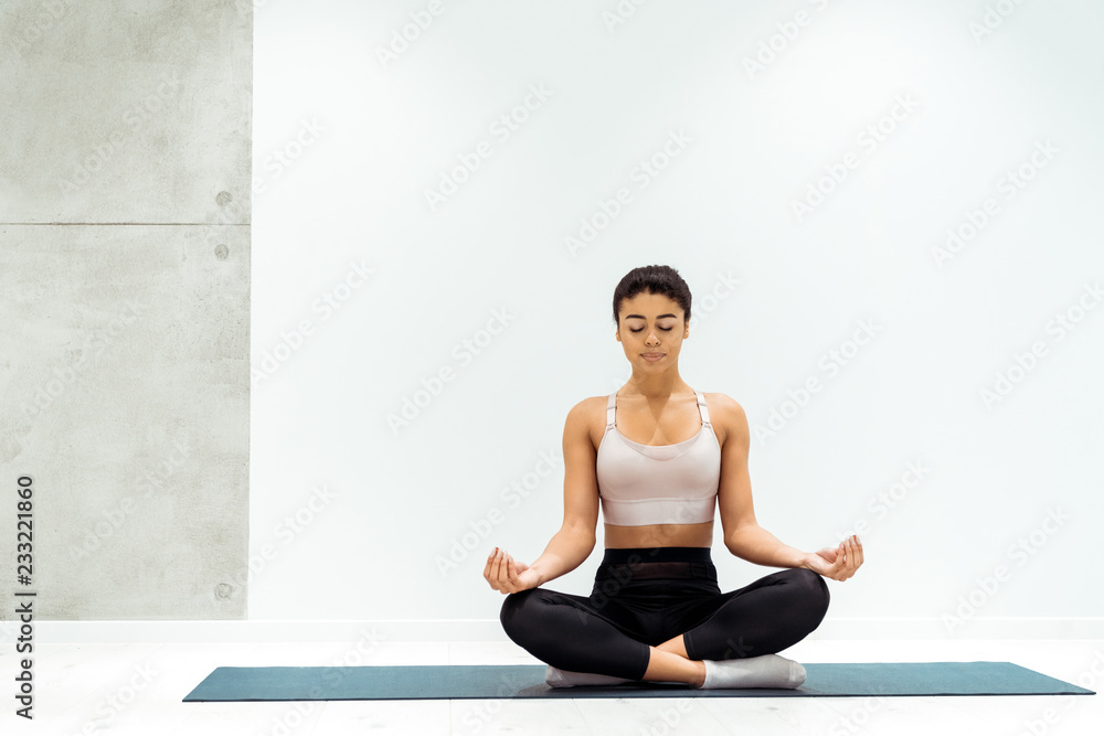 Relaxed girl with closed eyes meditating in lotus position in yoga studio Relaxed girl with closed eyes meditating in lotus position in yoga studio