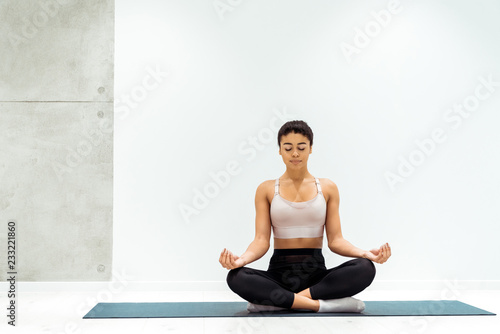 Relaxed girl with closed eyes meditating in lotus position in yoga studio