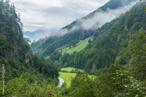 Billede på lærred Green Alpine valley after rain with the clouds raising over the forest with the