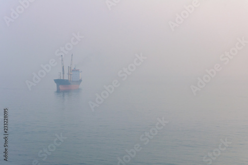 View of the cargo ship floating on the sea through the thick fog