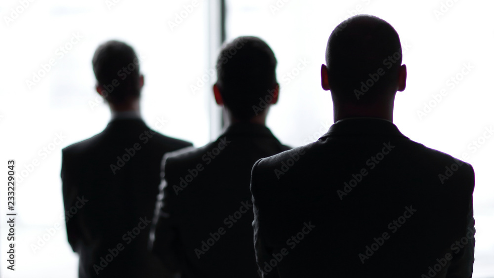 back view three employees as they look out on a large window overlooking the city back view three employees as they look out on a large window overlooking the city