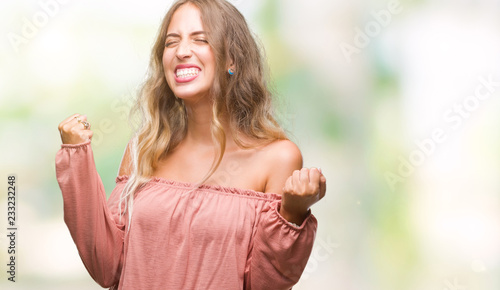 Beautiful young blonde woman over isolated background very happy and excited doing winner gesture with arms raised, smiling and screaming for success. Celebration concept.