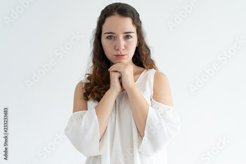 Portrait of serious young woman standing with her hands clasped. Caucasian woman praying or asking about something. Wishing concept