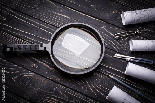 Magnifier, compasses and rolls from the drawing on a black wooden background photo