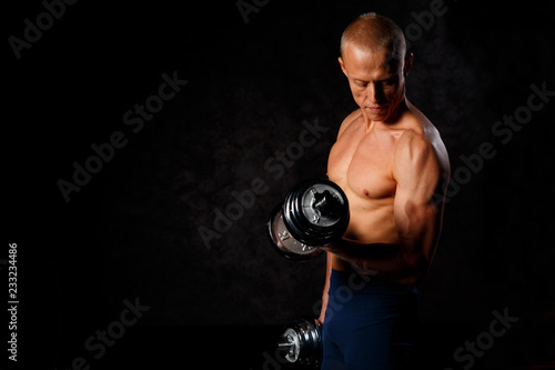 Handsome, muscular man with dumbbell over dark background.