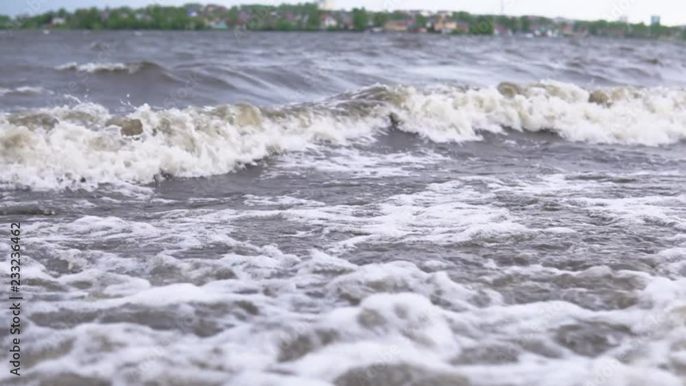 Dark muddy waves with white foam on the pebble beach after the storm, slow motion. Dark muddy waves with white foam on the pebble beach after the storm, slow motion.