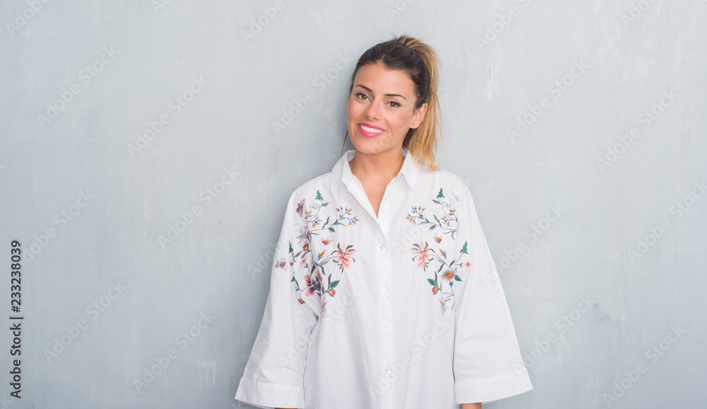 Young adult woman over grunge grey wall wearing flowers shirt with a happy and cool smile on face. Lucky person. Young adult woman over grunge grey wall wearing flowers shirt with a happy and cool smile on face. Lucky person.