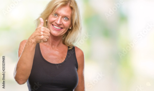 Middle age blonde woman over isolated background doing happy thumbs up gesture with hand. Approving expression looking at the camera with showing success.