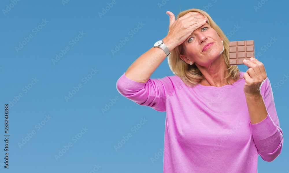 Middle age blonde woman eating chocolate bar over isolated background stressed with hand on head, shocked with shame and surprise face, angry and frustrated. Fear and upset for mistake. Middle age blonde woman eating chocolate bar over isolated background stressed with hand on head, shocked with shame and surprise face, angry and frustrated. Fear and upset for mistake.