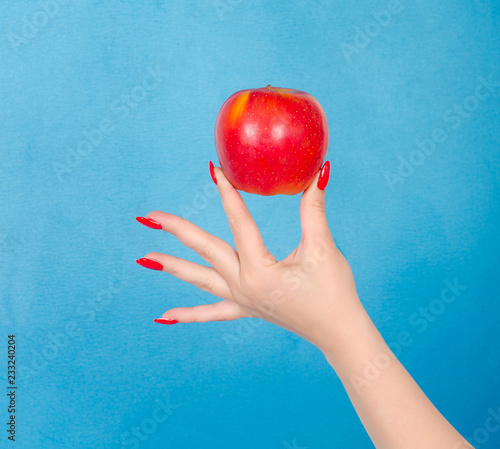 Red apple in the palm of the hand of a young woman on a blue background close-up