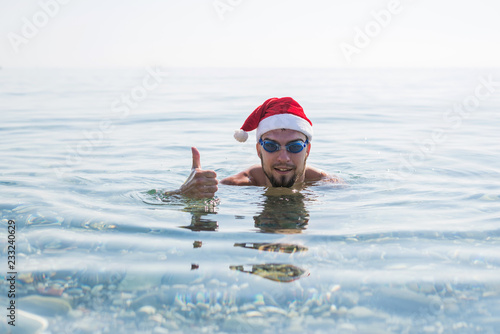 Man in a santa claus hat and swimming goggles thumbs up, christmas background. © mihakonceptcorn