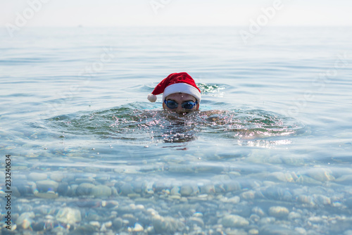 Man in a Santa Claus hat and glasses for swimming, christmas background. © mihakonceptcorn