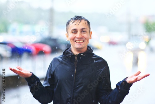 Portrait of a laughing man in a raincoat enjoing rain. He catches raindrops with his palms. Bad stormy rainy weather concept. Waterproof wear concept.
