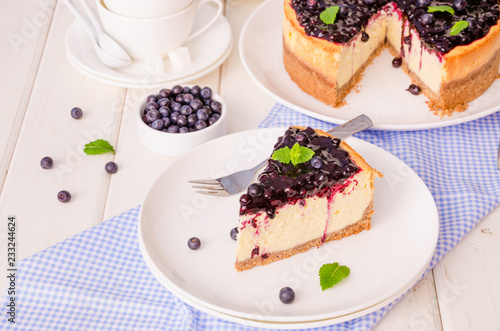 Delicious cream cheesecake with lemon zest and blueberry jam on a plate on a white wooden background