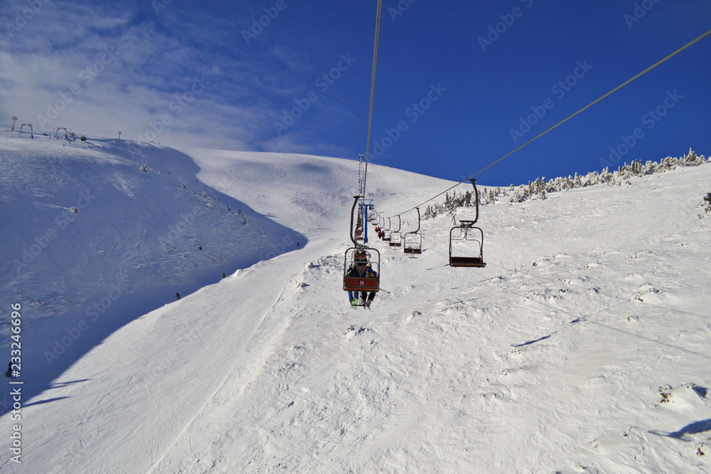 Snow covered colorful mountain landscape with ski lift, active young peoples and trees. Winter wiew from the lift up mountain. Landscape