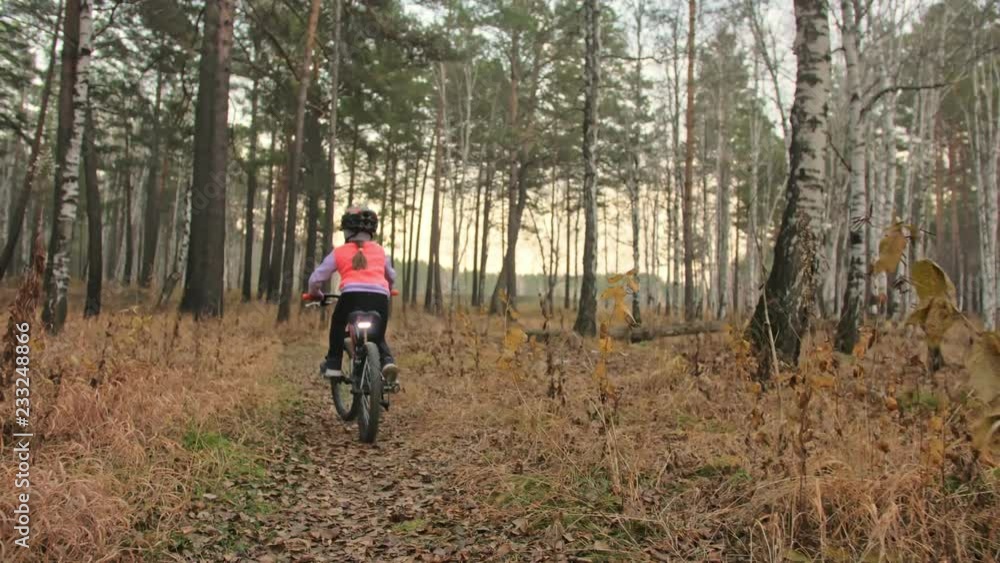 One caucasian children rides bike road in autumn park. Little girl riding black orange cycle in forest. Kid goes do bicycle sports. Biker motion ride with backpack and helmet. Mountain bike hardtail. One caucasian children rides bike road in autumn park. Little girl riding black orange cycle in forest. Kid goes do bicycle sports. Biker motion ride with backpack and helmet. Mountain bike hardtail.