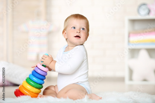 Baby boy with toys sitting on carpet at home