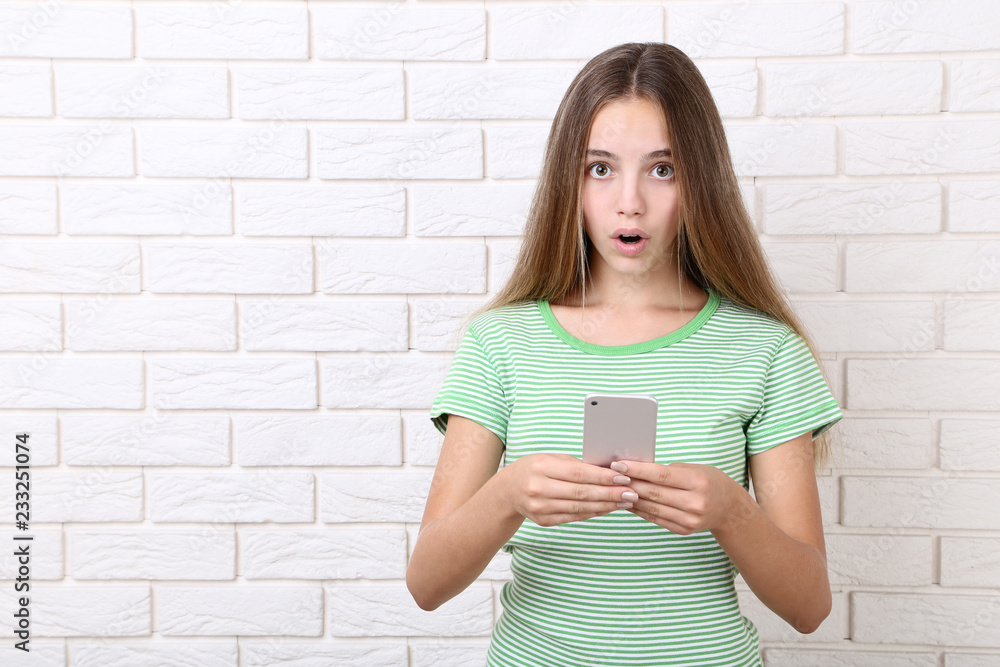 Surprised girl with smartphone on brick wall background Surprised girl with smartphone on brick wall background