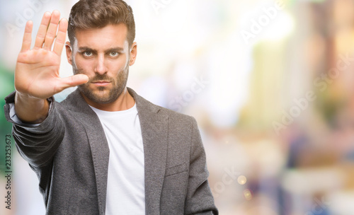 Young handsome business man over isolated background doing stop sing with palm of the hand. Warning expression with negative and serious gesture on the face.