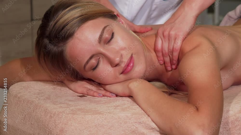 Young happy woman receiving relaxing back massage at the salon. Gorgeous woman smiling joyfully while having her body massaged by professional spa therapist. Recreation concept. Young happy woman receiving relaxing back massage at the salon. Gorgeous woman smiling joyfully while having her body massaged by professional spa therapist. Recreation concept.
