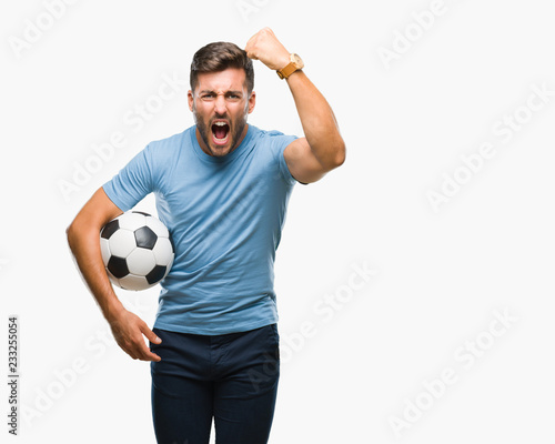 Fototapeta Naklejka Na Ścianę i Meble -  Young handsome man holding soccer football ball over isolated background annoyed and frustrated shouting with anger, crazy and yelling with raised hand, anger concept