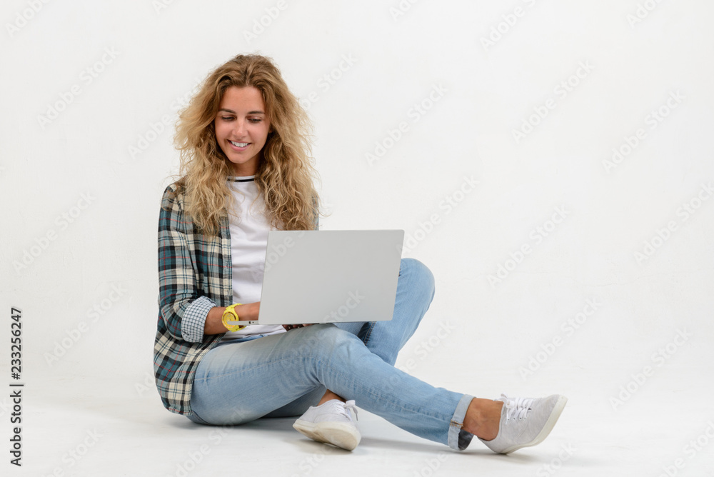Beautiful blonde woman sitting on floor with laptop on white background Beautiful blonde woman sitting on floor with laptop on white background