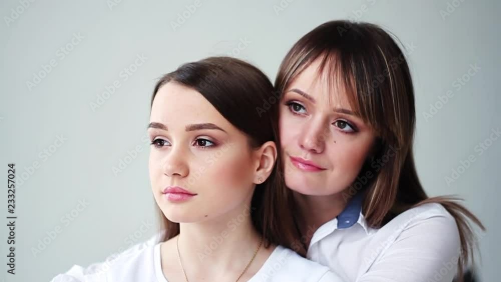 Charming beautiful young mother with her daughter stand hug look to side smile happy in studio white background attractive family female conversation cute girl close up portrait slow motion Charming beautiful young mother with her daughter stand hug look to side smile happy in studio white background attractive family female conversation cute girl close up portrait slow motion