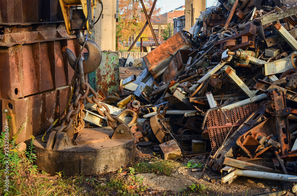 A crane with a hook on a chain hung a huge iron load for heavy lifting construction next to a dump of metal waste and products A crane with a hook on a chain hung a huge iron load for heavy lifting construction next to a dump of metal waste and products