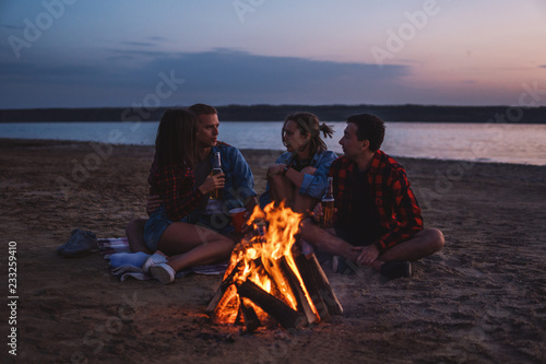 Camp on the beach. Group of young friends having picnic with bonfire. They drink beer