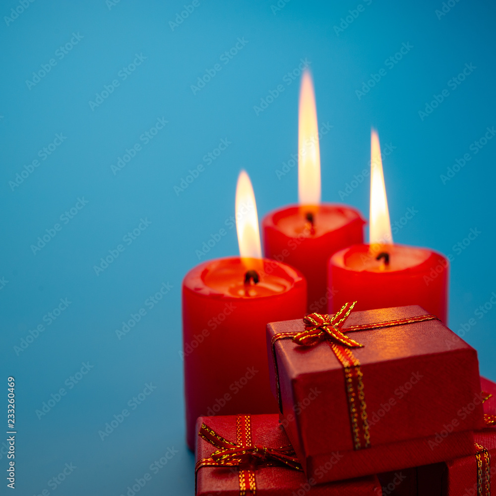 Three burning red candles and Christmas boxes on a blue background. Three burning red candles and Christmas boxes on a blue background.