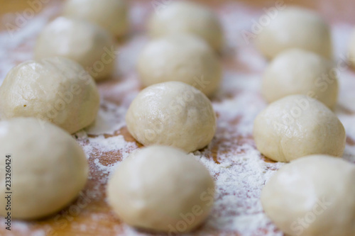 A close-up of small, white balls of home-made dough for a multi-layered banitsa and pizza on a kitchen table, flour for kneading. Shallow depth of focus.
