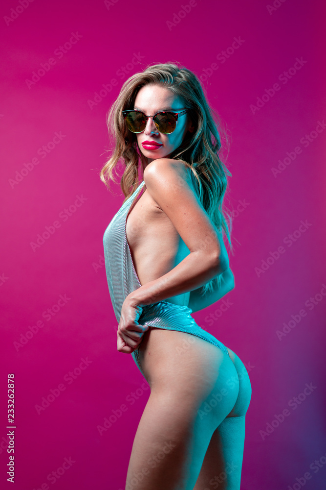 Obraz premium Hot woman in silver body suit with sunglasses on a purple magenta background with blue lights