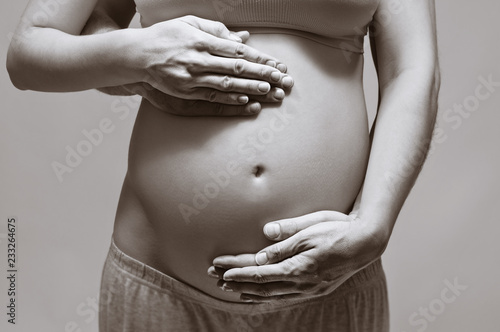 Black and white image of a beautiful pregnant woman. She and her husband hugging the tummy. Concept of happy pregnancy.