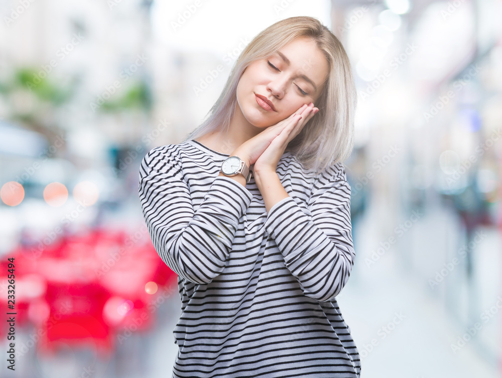 Young blonde woman over isolated background sleeping tired dreaming and posing with hands together while smiling with closed eyes.