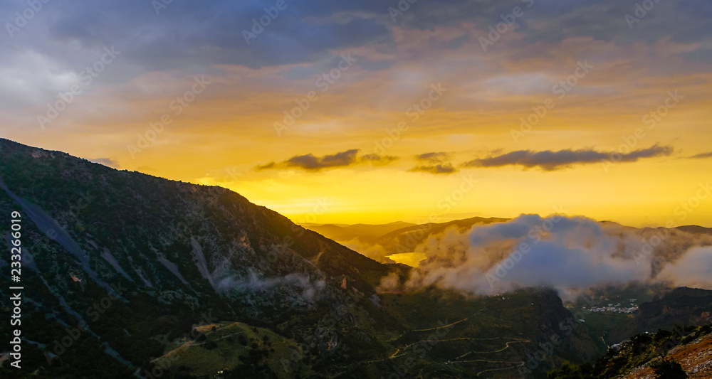 Picturesque mountain valley filled with curly clouds at sunset.