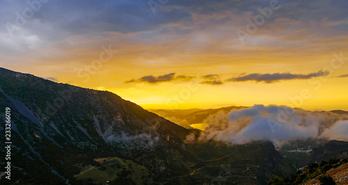 Picturesque mountain valley filled with curly clouds at sunset.