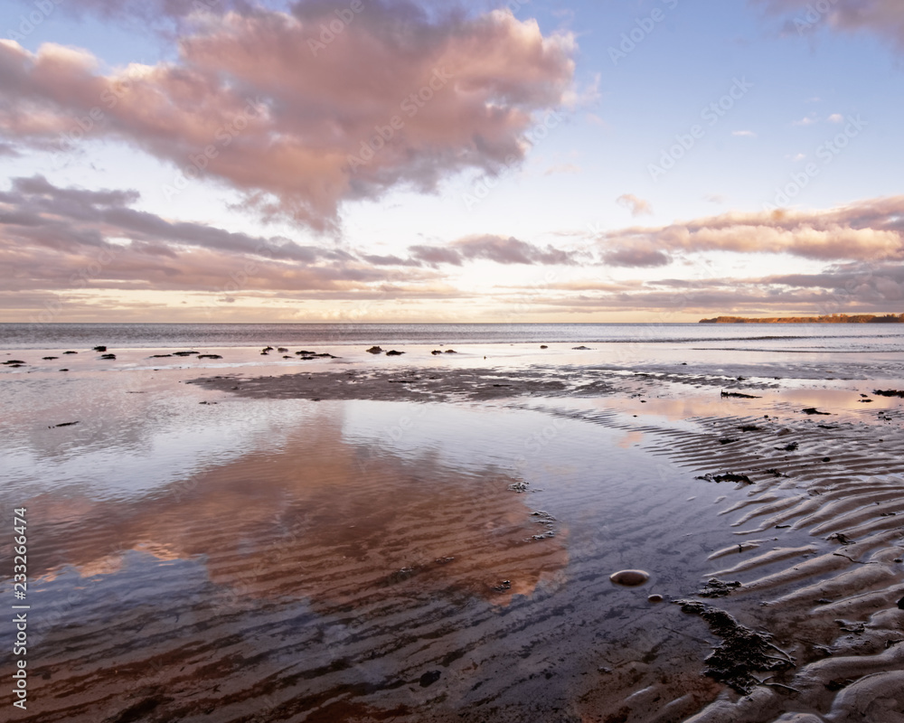 Scenic view over a coastal landscape, in the foreground sand ribs, above it some colored clouds, which are reflected in the shallow water - Location: Baltic Sea coast Island Ruegen, Germany