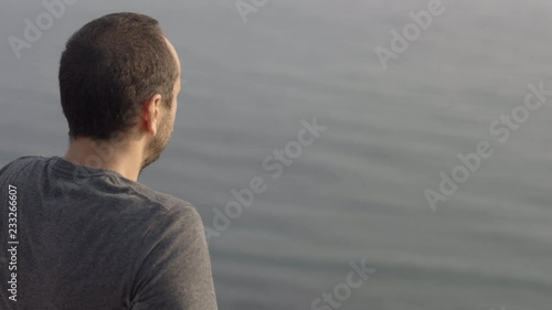 Young Man Sits On The Edge Of The Cliff Looking On The Sea - The Over The Shoulder