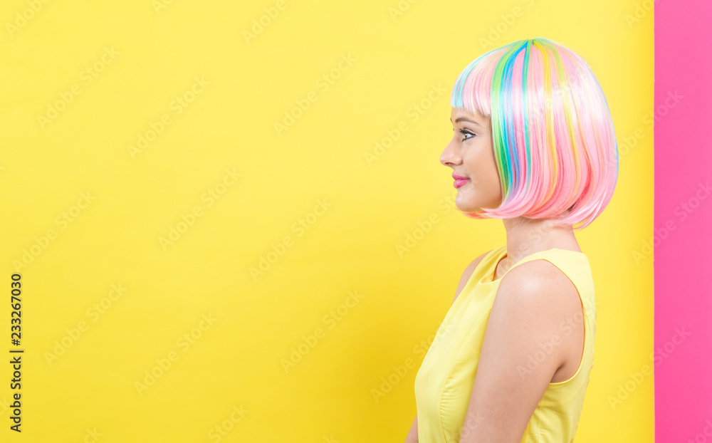 Beautiful woman in a bright colorful wig on a split yellow and pink background - obrazy, fototapety, plakaty 