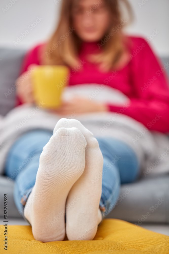 Obraz premium Sick girl holding cup and drinking coffee / tea on a couch.