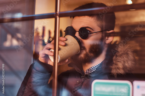 A handsome young stylish man drinking coffee in the cafe behind the window.
