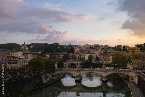 View of busy traffic on bridge Vittorio Emanuele, Gianicolo hill with buildings and trees, located between Trastevere and Vatican. Shot from Castel San Angelo during sunset.