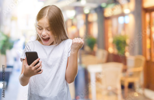 Young beautiful girl sending message texting using smarpthone over isolated background screaming proud and celebrating victory and success very excited, cheering emotion