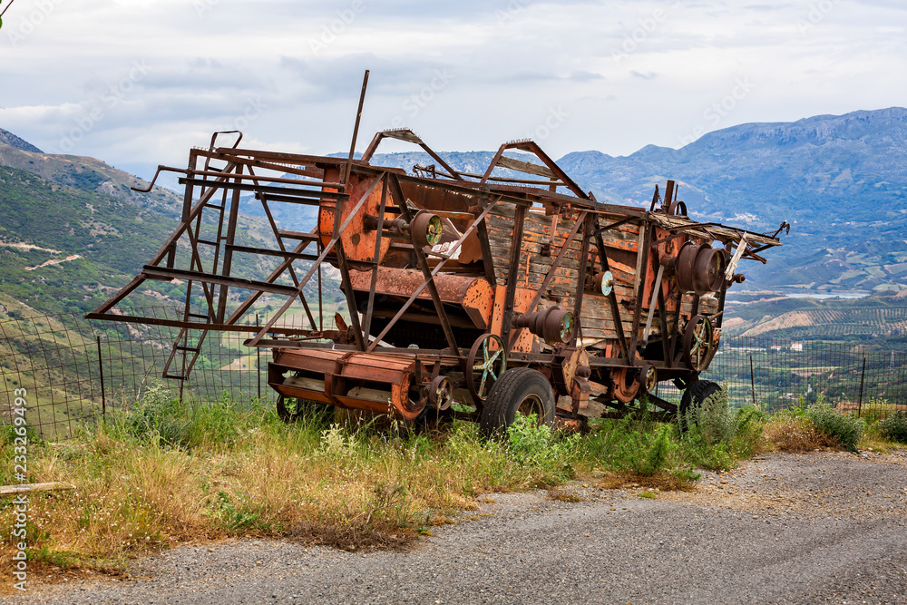 Fototapeta premium rusting and decaying combine harvester abandoned on mountain roadside with dramatic mountains behind.