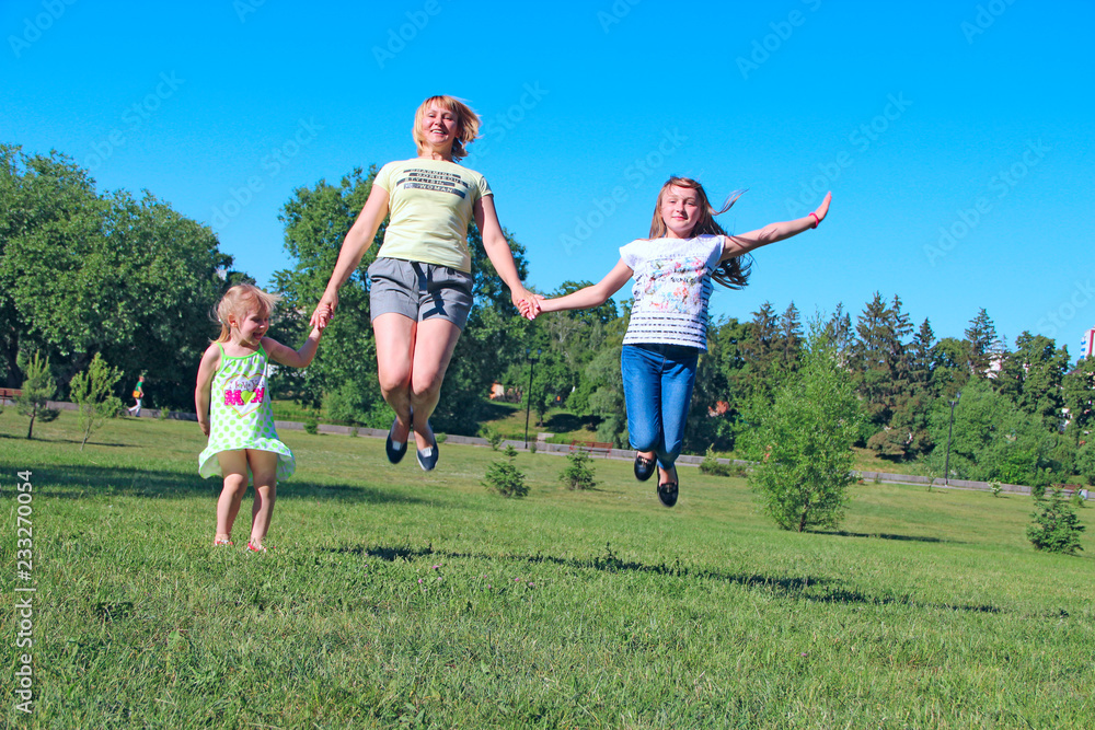 Happy mother having fun jumping with her daughters on green grass Happy mother having fun jumping with her daughters on green grass