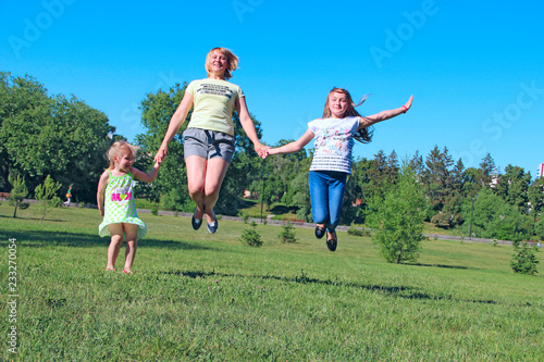 Happy mother having fun jumping with her daughters on green grass